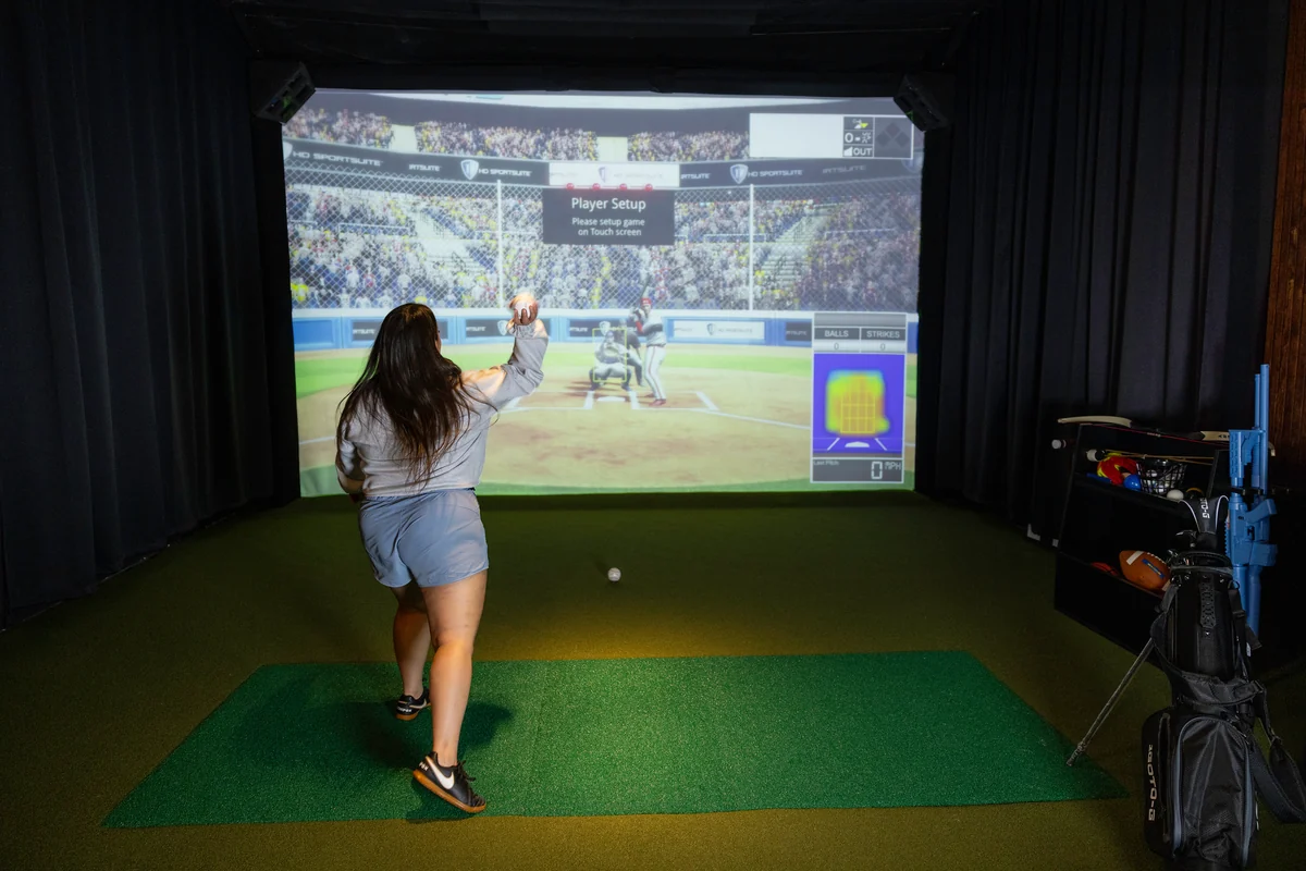 A guest throws a ball toward the baseball simulator in a PSC sports suite
