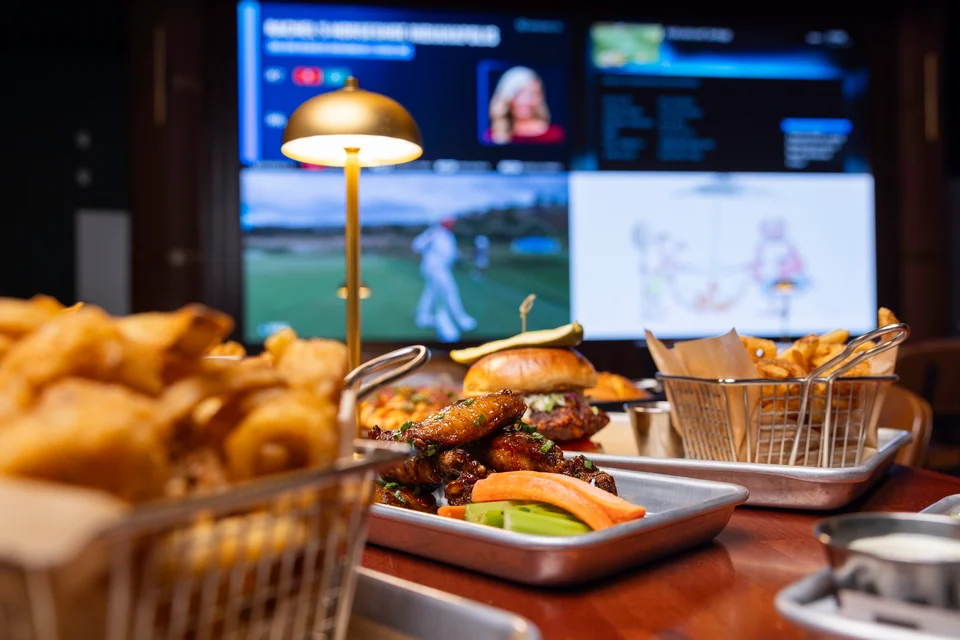 Wings, a burger and fries on a PSC table with sports playing beyond