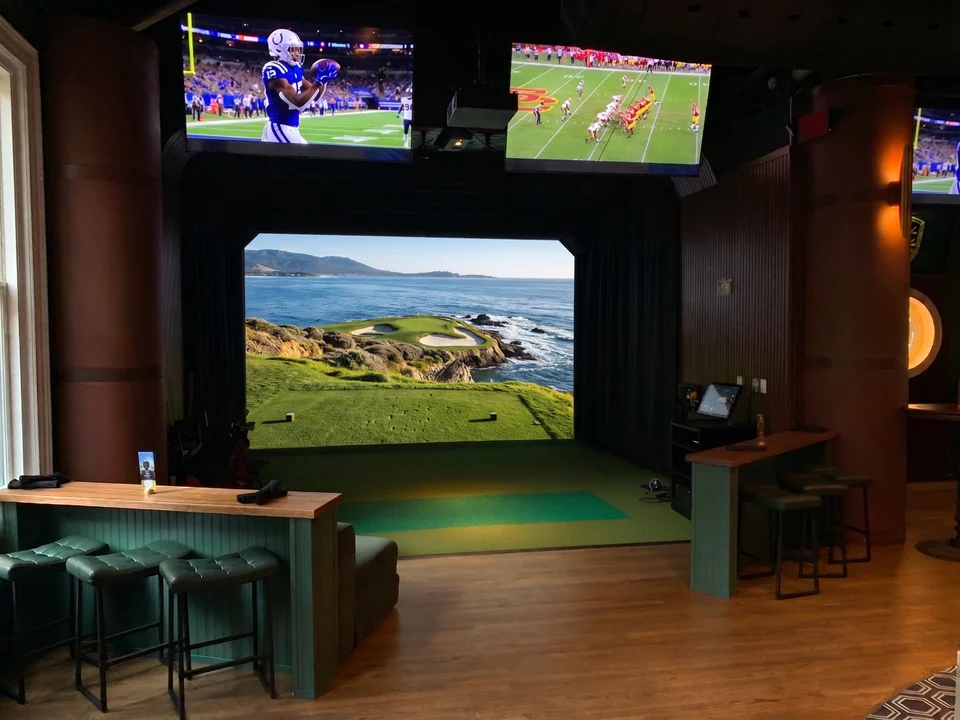 A PSC golf simulator bay beneath televisions showing football